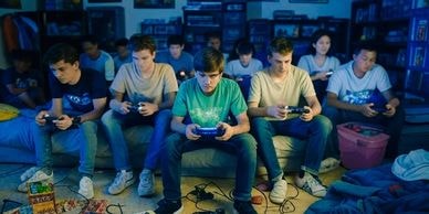 A group of boys and girls holding video game consoles in a dark room, looking intense